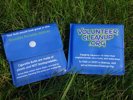 Branded reusable portable ashtray pouches in the grass, printed for VolunteerCleanup.org